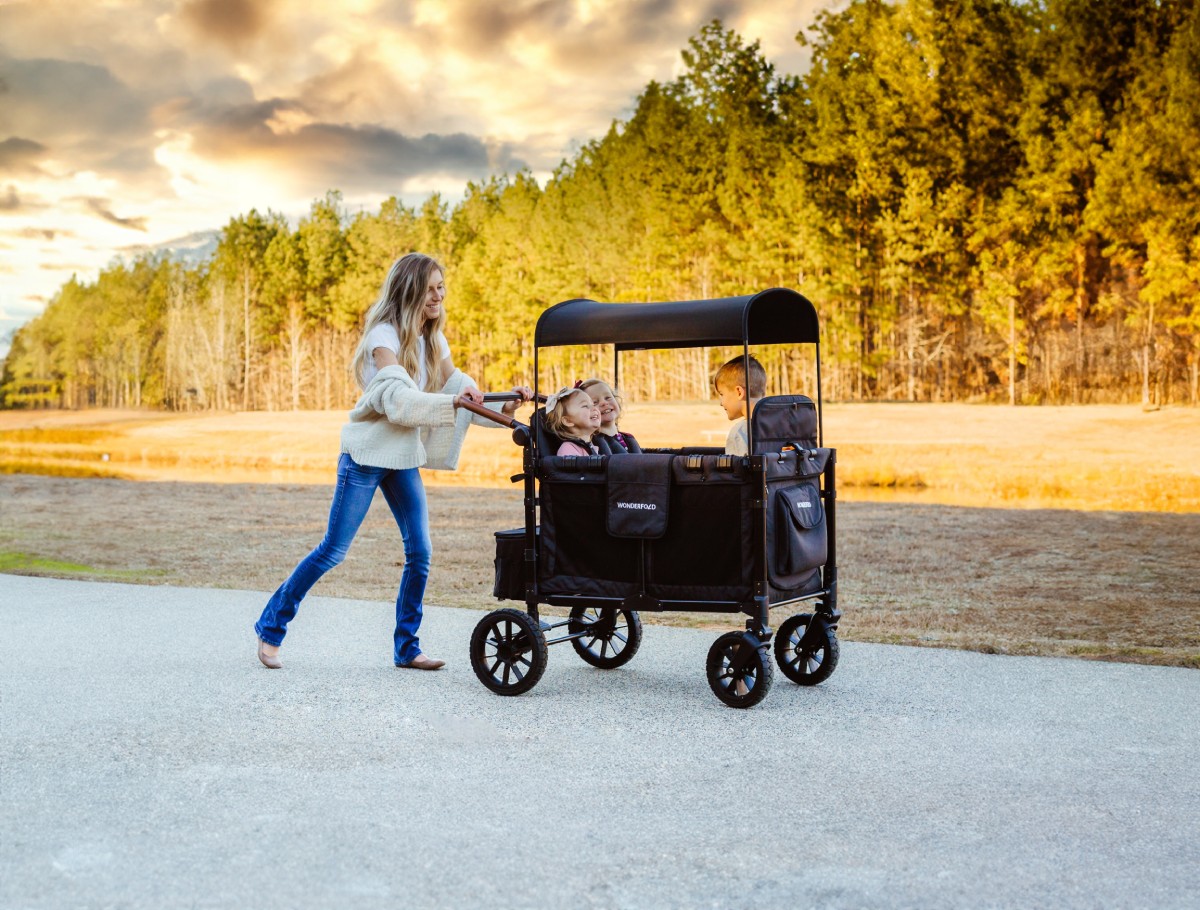 A woman pushing three children in a WonderFold W Series stroller wagon.