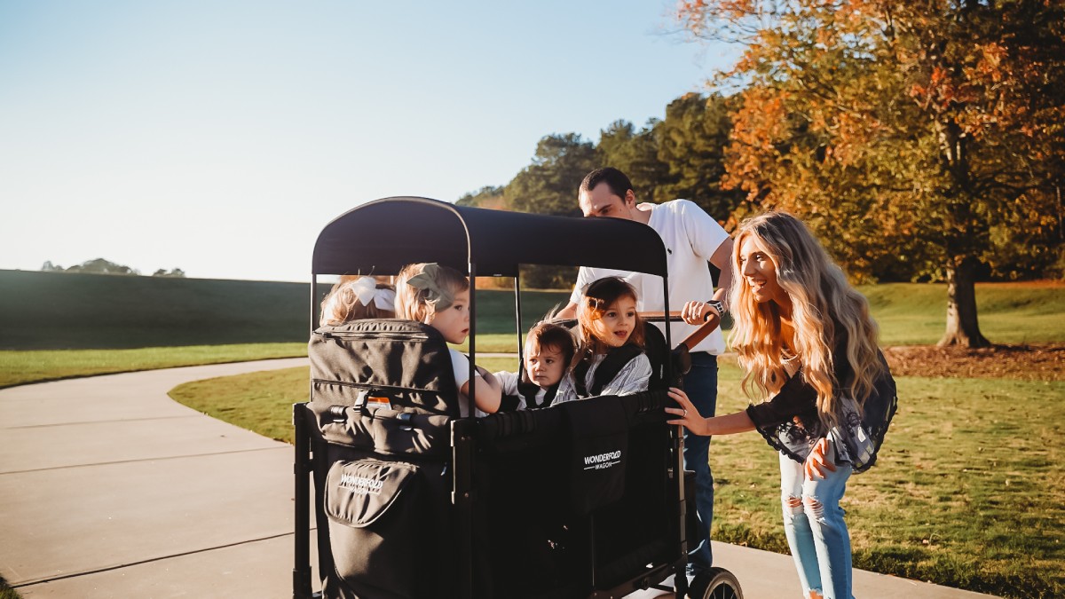 A family pushing four children in a WonderFold W4 Elite Pro in a park.